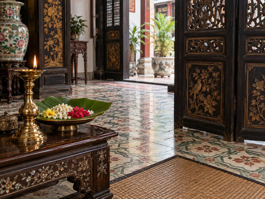 A Melaka shophouse interior with patterned tiles, a carved screen, a brass lamp and flowers on a banana leaf