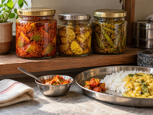Jars of mango, lime and green chilli pickle with a spoonful served beside rice and dal