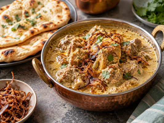 Mutton korma in a pale creamy gravy topped with fried onions, naan beside it